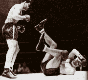 Louis stands up over a defeated Schmeling. Schmeling is toppled over on his back like a baby, his legs up in  the air.