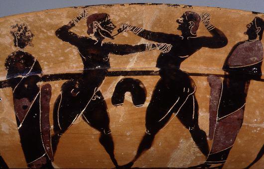 A red terracotta Greek bowl showing a bearded man defeating a clean shaven man in a boxing match. Their fists are wrapped in cloth, but otherwise they stand naked.  Their penises are small indeed.  Ha Ha Ha.